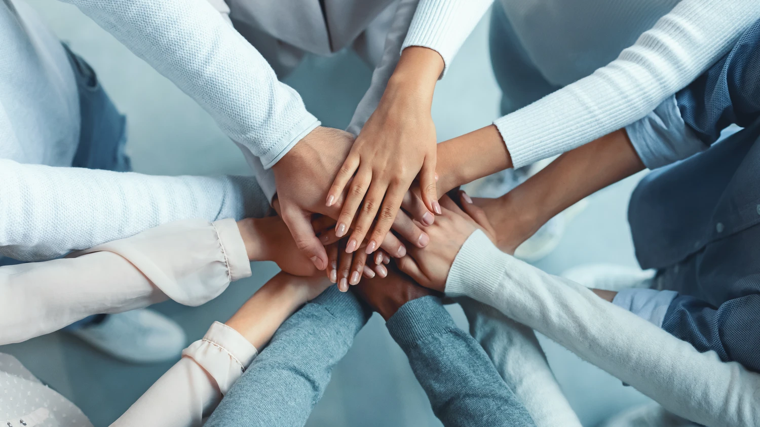 Europe Cleaning Service Bernd Leibold e.K. – Draufsicht auf ein multikulturelles Team, das durch das Übereinanderlegen der Hände seine Zusammenarbeit demonstriert.
